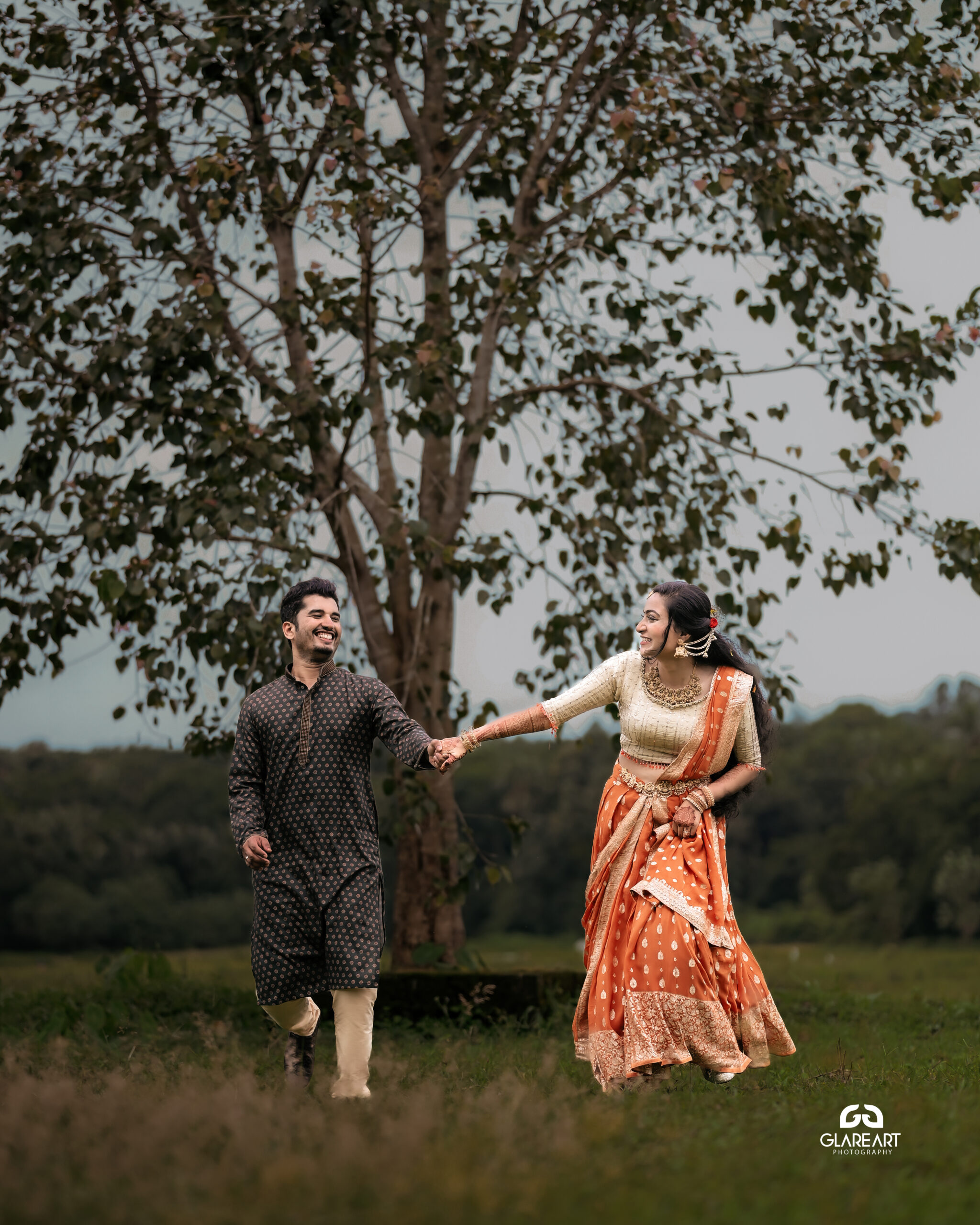 This is a lovely engagement-style photograph set in a natural outdoor location. The scene captures joyful and candid moments, emphasizing cultural attire- best wedding photography in Palakkad-wedding photography Palakkad