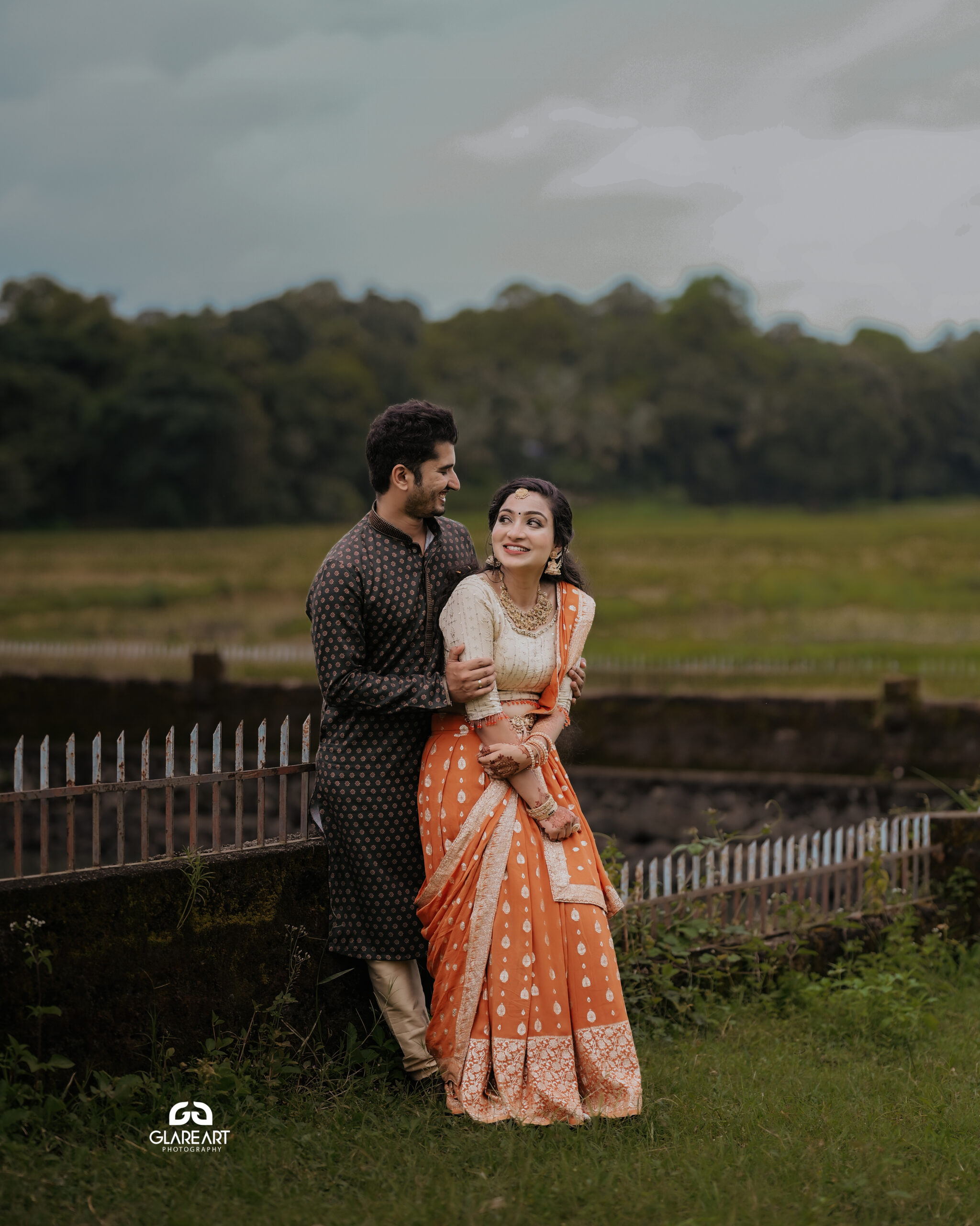 This is a lovely engagement-style photograph set in a natural outdoor location. The scene captures joyful and candid moments, emphasizing cultural attire- best wedding photography in Palakkad-wedding photography Palakkad