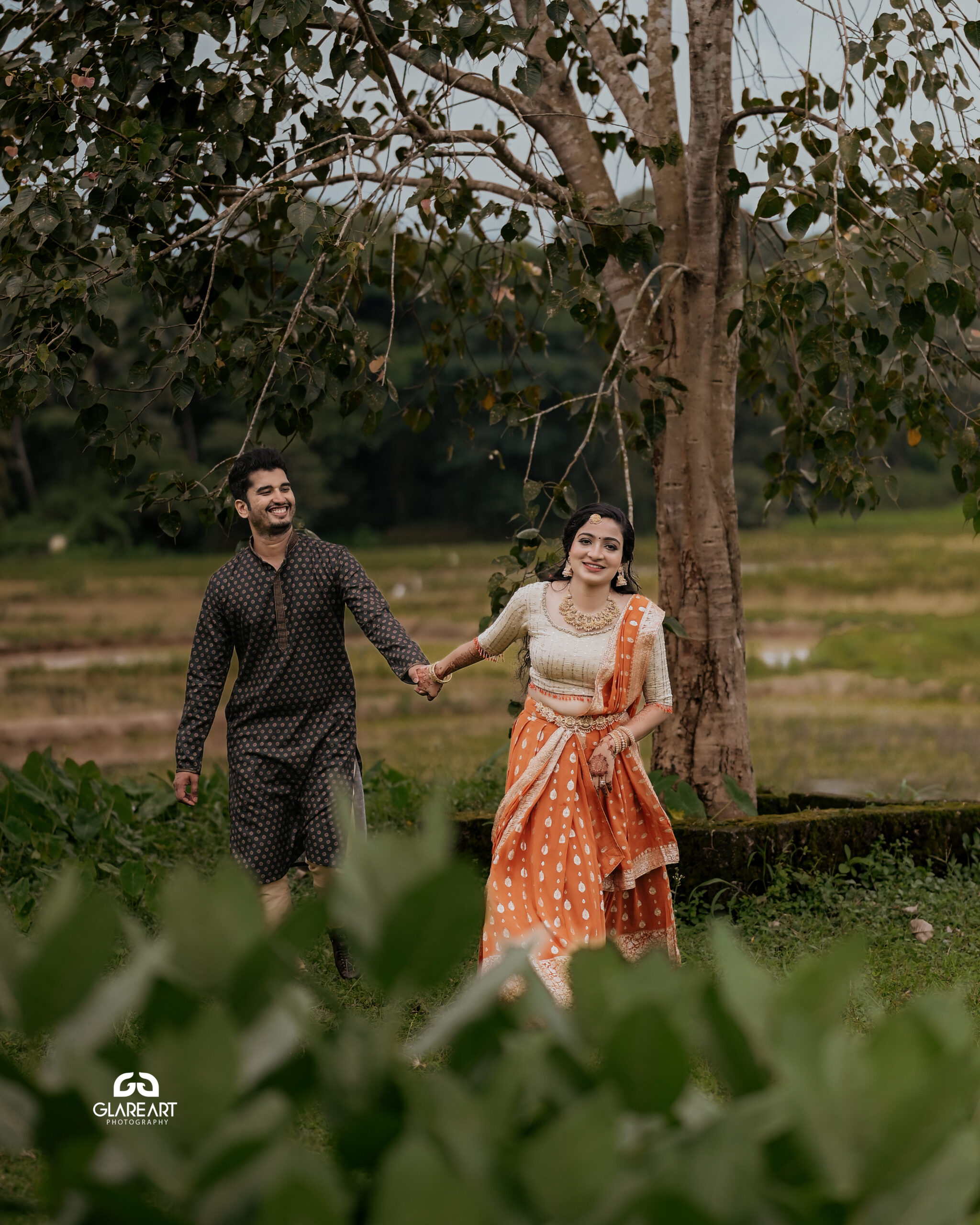 This is a lovely engagement-style photograph set in a natural outdoor location. The scene captures joyful and candid moments, emphasizing cultural attire- best wedding photography in Palakkad-wedding photography Palakkad