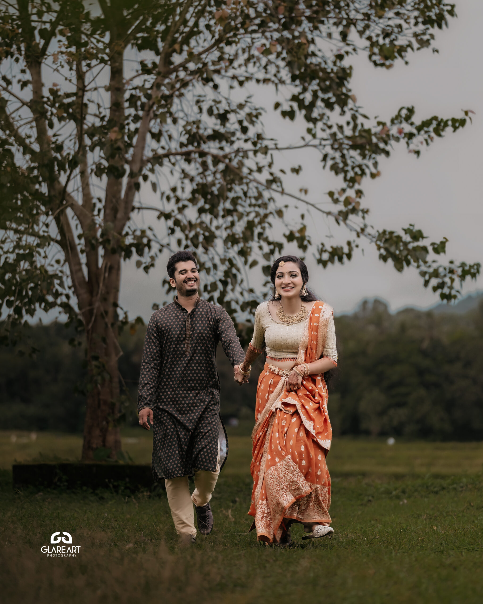 This is a lovely engagement-style photograph set in a natural outdoor location. The scene captures joyful and candid moments, emphasizing cultural attire- best wedding photography in Palakkad-wedding photography Palakkad